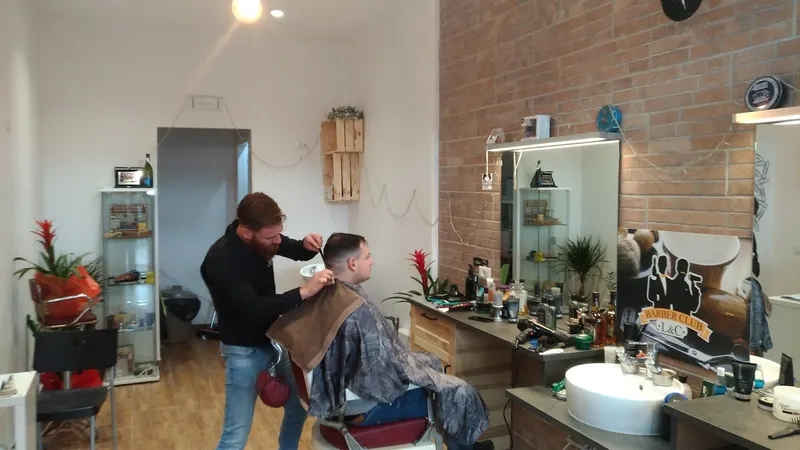 Luca al lavoro in salone: poltrona da barbiere, muro di mattoni, specchio e l'insegna Barber Club L&C